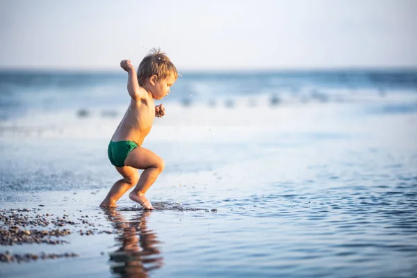 少し面白い子供 明るい休暇に暑い夏の太陽の下で砂の底に穏やかな青い海のシェルと小石を収集します — ストック写真