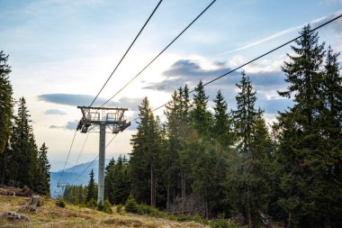 Güçlü ve güvenilir metal kablolu modern turist asansörü, Rodop Dağları 'nın dağ sıralarının arka planında, uzun tüylü, dikenli köknar ağaçlarıyla sonsuz yeşil ladin bahar ormanlarının arasından geçer.