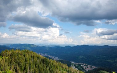 Yoğun koyu ladin ormanları ve mavi bulutlu gökyüzü ile kaplı dağ vadisinin arka planına karşı yeşil parlak bitki örtüsüyle kaplı Rodop Dağlarının yüksek kayalık vahşi dağ sıraları
