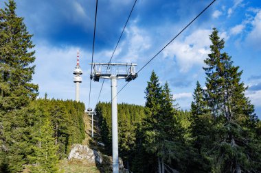 Güçlü ve güvenilir metal kablolu modern turist asansörü, Rodop Dağları 'nın dağ sıralarının arka planında, uzun tüylü, dikenli köknar ağaçlarıyla sonsuz yeşil ladin bahar ormanlarının arasından geçer.