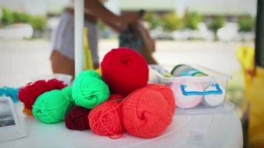 Bir çok büyük iplik ve kurdele parlak renkli neşeli çiçeklerle plastik beyaz bir masanın üzerinde uzanır, küçük zarif bir kızın arka planında mavi Afrika örgüleri örgü örüyor