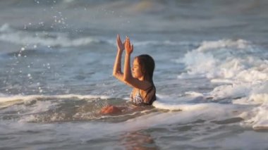 Parlak leopar bikinili, ıslak saçlı neşeli kız. Etrafına su sıçratıyor ve mavi yaz denizinde otururken sıcak güneşin tadını çıkarıyor.