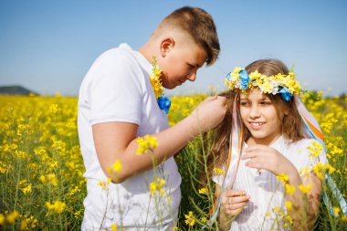 Önemseyen ağabeyi, parlak Ukrayna çiçek çelenkleriyle çok renkli ince kurdeleler örüyor. Küçük, gülümseyen kız kardeşin başında. Açık mavi gökyüzünün altında bitmeyen kolza tohumu tarlasında.