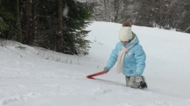 Şiddetli rüzgar eserken, plastikten kızağını yukarı çeken bir kadının ön görüntüsü. Mavi ceketli güzel kız arka planda kayak yapan bir adamla karlı tepeye tırmanıyor. Kış sporu kavramı.