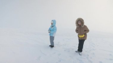Sisli bir sabah karlı yamaçta el ele yürüyen iki çocuğun yan görüntüsü. Kar tepesinde yürüyüş yapan kız kardeşler fotokopi alanı ve ışık arkaplanı olan manzarayı keşfediyorlar. Kış yürüyüşü kavramı.