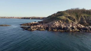 Bulgaristan 'ın parlak güneşli akşam günbatımına karşı sakin, mavi yansıtıcı Karadeniz ve eski karanlık kayalık taşlarla kaplı deniz manzarası. UHD 4K video gerçek zamanlı