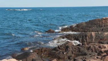 Bulgaristan 'ın parlak güneşli günbatımı ışığı altında, Karadeniz' in yansıtıcı ilkbaharı yakınlarında, koyu nemli deniz kumları ve büyük ıslak kayalık kayalıkları olan vahşi bir taş ve kumlu bir sahil. 4K UHD yavaş çekim videosu