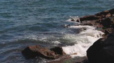 Bulgaristan 'ın parlak güneşli günbatımı ışığı altında, Karadeniz' in yansıtıcı ilkbaharı yakınlarında, koyu nemli deniz kumları ve büyük ıslak kayalık kayalıkları olan vahşi bir taş ve kumlu bir sahil. 4K UHD yavaş çekim videosu