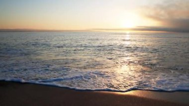Sakin mavi uçsuz bucaksız Karadeniz, ışığı yansıtan soğuk su ve yakındaki kumlu boş kumsal, bulutlu renkli gökyüzüne karşı beyaz bulutlar ve parlak şafak güneşi. UHD 4K video yavaş çekim