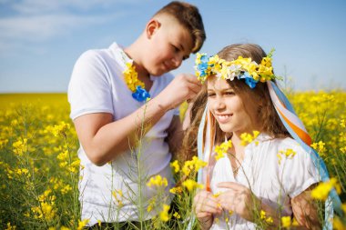 Önemseyen ağabeyi, parlak Ukrayna çiçek çelenkleriyle çok renkli ince kurdeleler örüyor. Küçük, gülümseyen kız kardeşin başında. Açık mavi gökyüzünün altında bitmeyen kolza tohumu tarlasında.