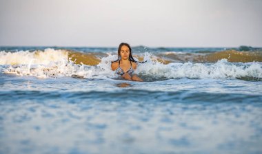 Parlak leopar bikinili, ıslak saçlı neşeli kız. Etrafına su sıçratıyor ve mavi yaz denizinde otururken sıcak güneşin tadını çıkarıyor.