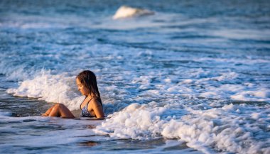 Parlak leopar bikinili, ıslak saçlı neşeli kız. Etrafına su sıçratıyor ve mavi yaz denizinde otururken sıcak güneşin tadını çıkarıyor.
