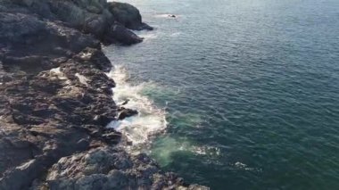 Bulgaristan 'ın parlak güneşli akşam günbatımına karşı sakin, mavi yansıtıcı Karadeniz ve eski karanlık kayalık taşlarla kaplı deniz manzarası. UHD 4K video gerçek zamanlı