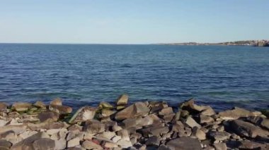 Bulgaristan 'ın parlak güneşli akşam günbatımına karşı sakin, mavi yansıtıcı Karadeniz ve eski karanlık kayalık taşlarla kaplı deniz manzarası. UHD 4K video gerçek zamanlı
