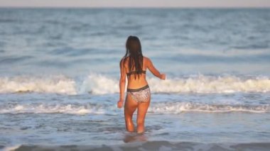 Siyah saçlı, şişman, dalgın ve esmer bir kız. Mavi sığ denizde yürüyor. Küçük dalgalarla ve ılık yaz güneşinin tadını çıkarıyor.