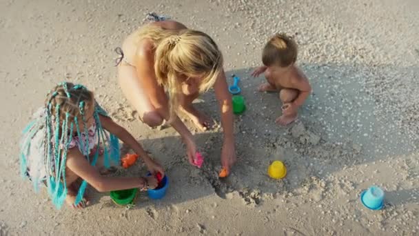 一位慈祥美丽的母亲和她的孩子们一起玩耍 大瘦小的女儿和最小的儿子蹒跚学步 用贝壳和鹅卵石装饰着珠子和沙堡 Uhd慢速视频 — 图库视频影像