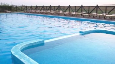 Sıcak, parlak bir günbatımının arka planına karşı yaz tatilinde, şeffaf, küçük ışık dalgaları ile serin, derin bir havuzun üst görüntüsü. 4K UHD yavaş çekim videosu