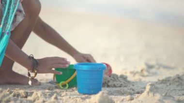 Bronzlaşmış, şevkli, parlak Afrika örgülü, yaz mevsiminde pembe takım elbiseli, deniz kenarında deniz kabukları ve ılık, güneşli, güneşli gün batımında köpüklü dalgalarla oynayan zayıf bir kız. 4K UHD yavaş çekim videosu