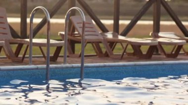 Sıcak, parlak bir günbatımının arka planına karşı yaz tatilinde, şeffaf, küçük ışık dalgaları ile serin, derin bir havuzun üst görüntüsü. 4K UHD yavaş çekim videosu