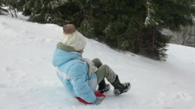 Side view of young girl speeding down snowy hill. Happy female kid, warmly dressed with coat and mittens, sledding down hill on feet with pine woodland on background. Concept of winter activities.