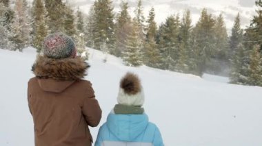 Back view of children staying along on slope, exploring magnificent landscape while frozen wind blowing. Two female kids in winter clothes looking at snow covered forest. Concept of winter hiking.