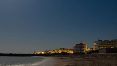 Seaside resort town of Pomorie with bright electric lights and large comfortable luxury hotels against background of night starry blue sky and calm cold Black Sea, in Bulgaria. 4K UHD timelapse video