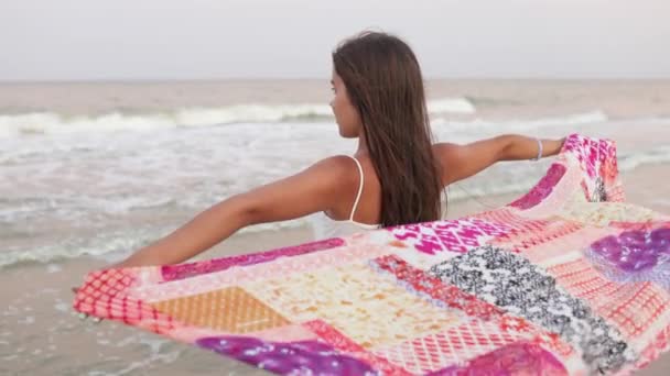 一个身穿雪白夏季T恤和米色短裤的胖胖的 梦幻般的黑发女孩正沿着沙滩散步 望着地平线 手里拿着明亮的披巾 — 图库视频影像
