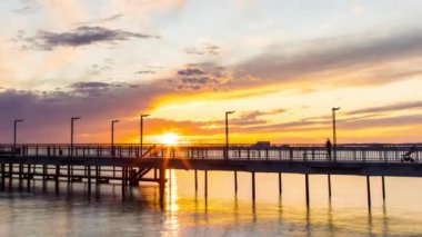 Side view of an old empty small pier on a calm quiet reflective Black Sea, against a cloudy multi-colored sky and a bright evening sunset. 4K UHD timelapse video