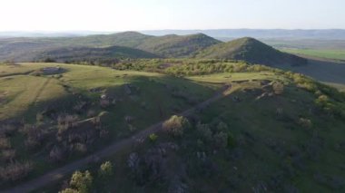 Birds eye view of spring blooming green meadows and wooded hilly slopes of the Balkan Mountains, under the light of a bright cloudy warm day in the country of Bulgaria. UHD 4K video realtime