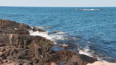 Bulgaristan 'ın parlak güneşli günbatımı ışığı altında, Karadeniz' in yansıtıcı ilkbaharı yakınlarında, koyu nemli deniz kumları ve büyük ıslak kayalık kayalıkları olan vahşi bir taş ve kumlu bir sahil. 4K UHD yavaş çekim videosu