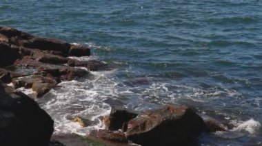 Bulgaristan 'ın parlak güneşli günbatımı ışığı altında, Karadeniz' in yansıtıcı ilkbaharı yakınlarında, koyu nemli deniz kumları ve büyük ıslak kayalık kayalıkları olan vahşi bir taş ve kumlu bir sahil. 4K UHD yavaş çekim videosu