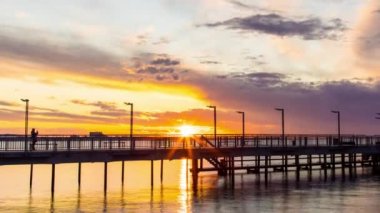 Side view of an old empty small pier on a calm quiet reflective Black Sea, against a cloudy multi-colored sky and a bright evening sunset. 4K UHD timelapse video