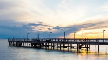 Side view of an old empty small pier on a calm quiet reflective Black Sea, against a cloudy multi-colored sky and a bright evening sunset. 4K UHD timelapse video
