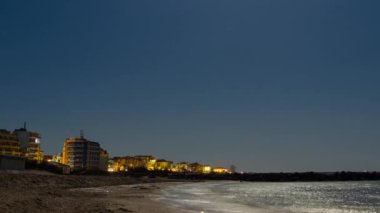 Seaside resort town of Pomorie with bright electric lights and large comfortable luxury hotels against background of night starry blue sky and calm cold Black Sea, in Bulgaria. 4K UHD timelapse video