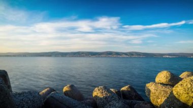 A small concrete reliable breakwater against the background of a spacious blue cloudy sky and a raging blue empty Black Sea, with white sea strong waves. 4K UHD timelapse video