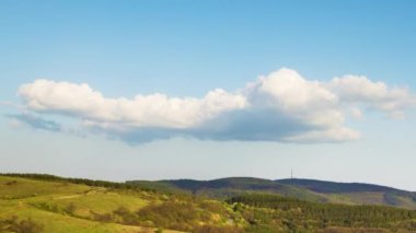 Valley with dry grassy green meadows with bare spring small bushes and big mighty colorful trees and low hilly Balkan mountains, under sky blue cloudy windy sky. 4K UHD timelapse video