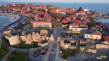 Bulgaristan 'ın Karadeniz kıyısındaki bir yarımadada yürüyen insanlarla dolu yeşil yay parkları ve dar caddelerle kaplı antik deniz kasabası Nesebar' a kuşların bakış açısı. UHD 4K video gerçek zamanlı