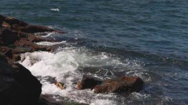 Bulgaristan 'ın parlak güneşli günbatımı ışığı altında, Karadeniz' in yansıtıcı ilkbaharı yakınlarında, koyu nemli deniz kumları ve büyük ıslak kayalık kayalıkları olan vahşi bir taş ve kumlu bir sahil. 4K UHD yavaş çekim videosu