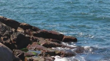 Bulgaristan 'ın parlak güneşli günbatımı ışığı altında, Karadeniz' in yansıtıcı ilkbaharı yakınlarında, koyu nemli deniz kumları ve büyük ıslak kayalık kayalıkları olan vahşi bir taş ve kumlu bir sahil. 4K UHD yavaş çekim videosu