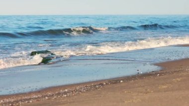 Sakin mavi uçsuz bucaksız Karadeniz, ışığı yansıtan soğuk su ve yakındaki kumlu boş kumsal, bulutlu renkli gökyüzüne karşı beyaz bulutlar ve parlak şafak güneşi. UHD 4K video yavaş çekim