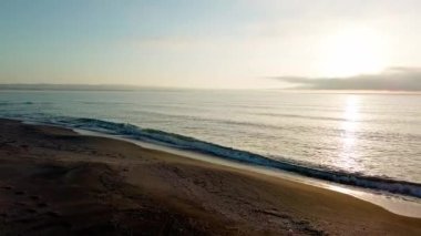 Sakin mavi uçsuz bucaksız Karadeniz, ışığı yansıtan soğuk su ve yakındaki kumlu boş kumsal, bulutlu renkli gökyüzüne karşı beyaz bulutlar ve parlak şafak güneşi. UHD 4K video gerçek zamanlı