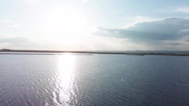 Boundless calm Black Sea with cool water reflecting light extends beyond the horizon, under colored sky with white volatile clouds and a bright dawn warm spring sun. UHD 4K video realtime