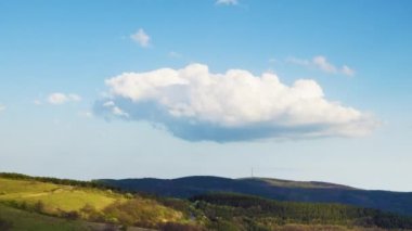 Valley with dry grassy green meadows with bare spring small bushes and big mighty colorful trees and low hilly Balkan mountains, under sky blue cloudy windy sky. 4K UHD timelapse video