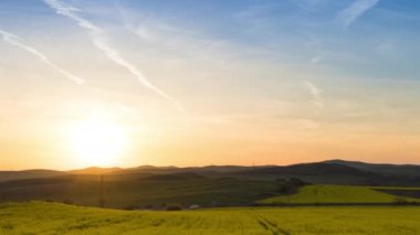 A large spring flowering field with bright yellow small plants in a mountain and meadow valley against the backdrop of a golden evening sunset sky, in warm country of Bulgaria. 4K UHD timelapse video