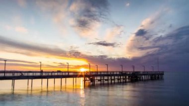Side view of an old empty small pier on a calm quiet reflective Black Sea, against a cloudy multi-colored sky and a bright evening sunset. 4K UHD timelapse video