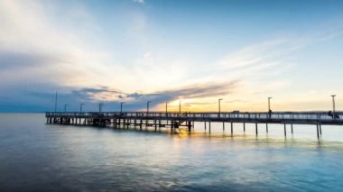 Side view of an old empty small pier on a calm quiet reflective Black Sea, against a cloudy multi-colored sky and a bright evening sunset. 4K UHD timelapse video