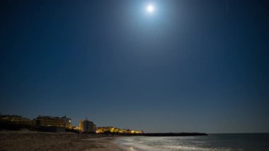 Seaside resort town of Pomorie with bright electric lights and large comfortable luxury hotels against background of night starry blue sky and calm cold Black Sea, in Bulgaria. 4K UHD timelapse video