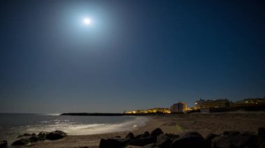 Seaside resort town of Pomorie with bright electric lights and large comfortable luxury hotels against background of night starry blue sky and calm cold Black Sea, in Bulgaria. 4K UHD timelapse video