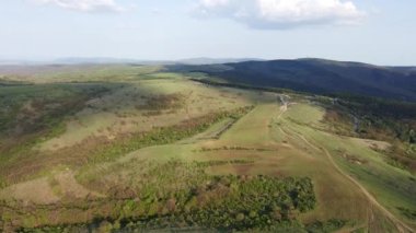 Birds eye view of spring blooming green meadows and wooded hilly slopes of the Balkan Mountains, under the light of a bright cloudy warm day in the country of Bulgaria. UHD 4K video realtime