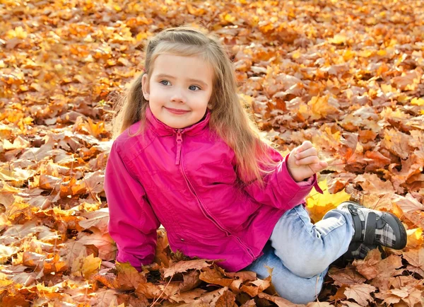 Portrait of cute little girl sitting in leaves — Stock Photo, Image